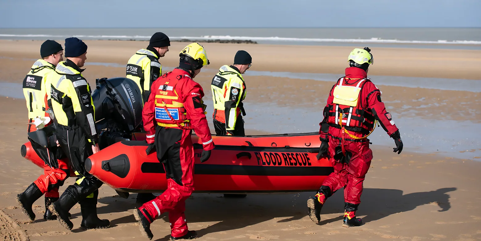 Rescue team carrying a red Gemini Marine Swift Water Rescue RIB across the beach